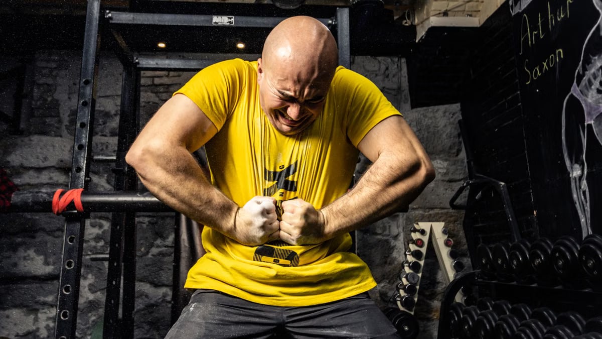 Bald muscular man in yellow t-shirt showcasing strength in a gym, highlighting intense dedication.